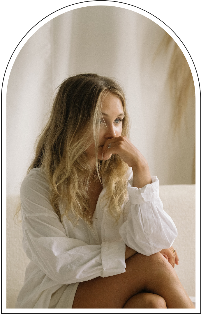 Blonde woman in a white shirt sitting on a sofa, resting her chin on her hand.