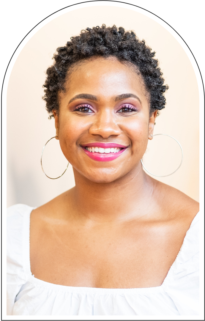 Smiling Black woman with short natural curls, hoop earrings, and bright pink lipstick wearing a white blouse