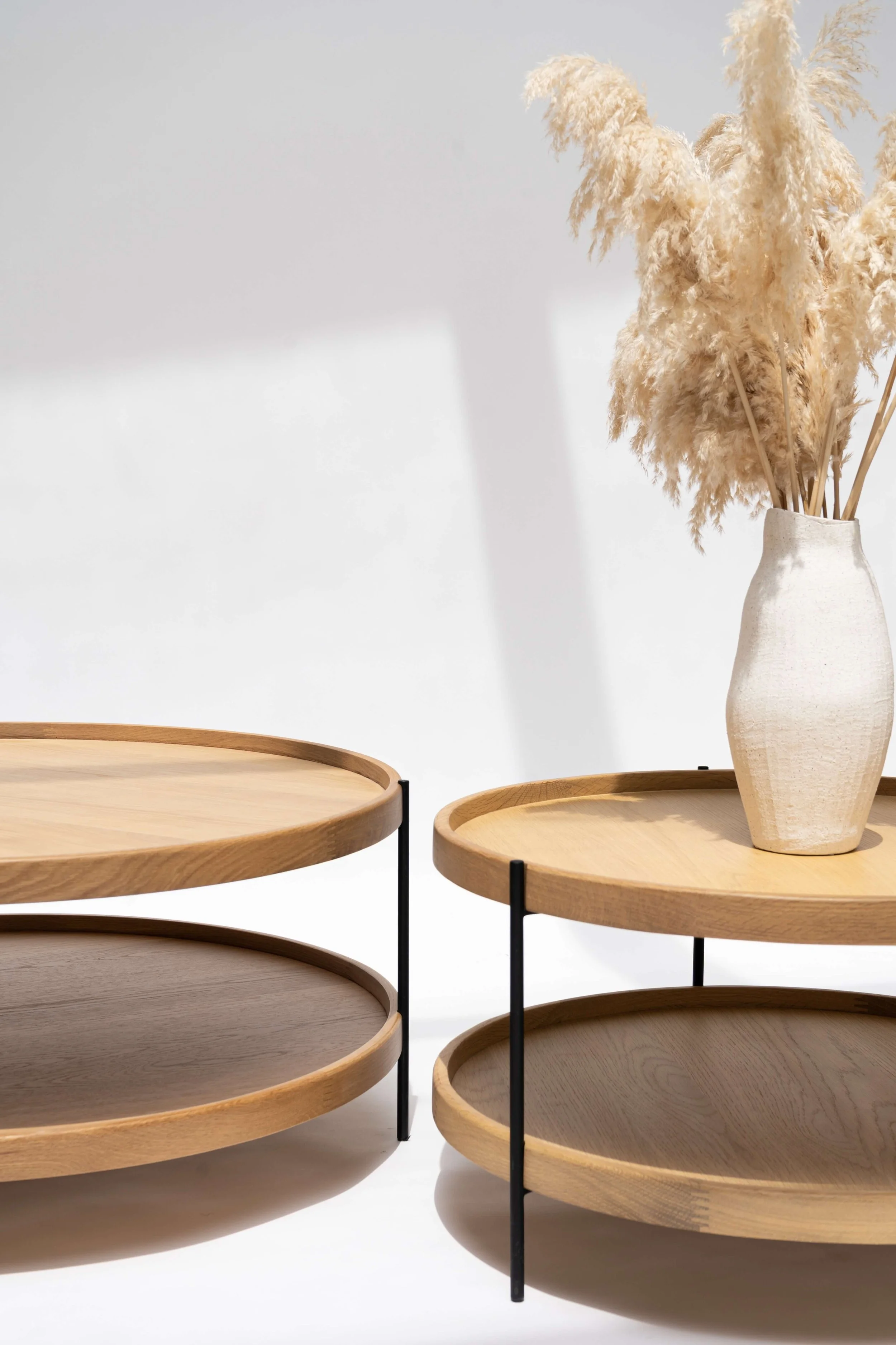 Modern round wooden nesting tables with black metal legs and a ceramic vase of dried pampas grass
