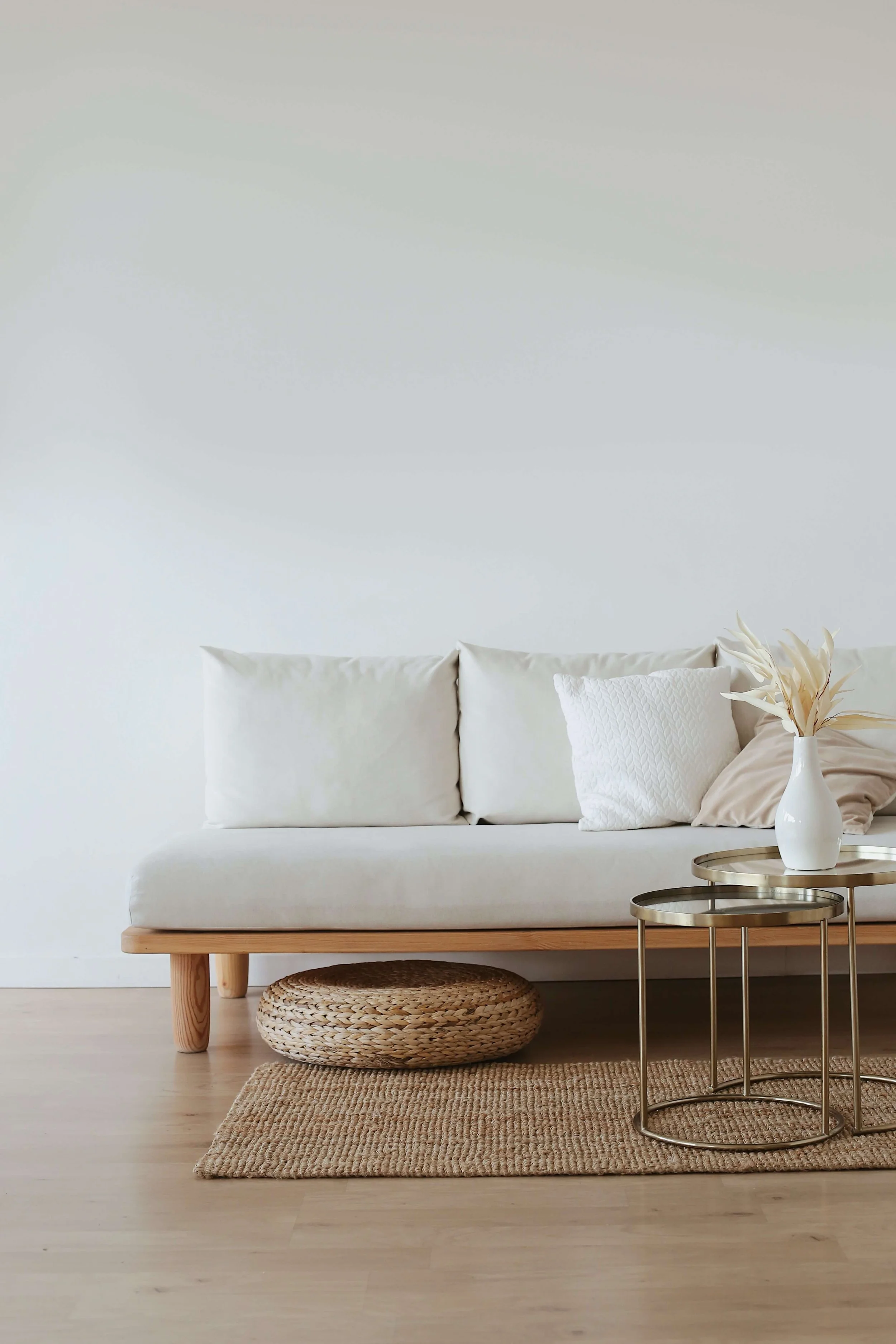 Bright minimalist living room with a white sofa, textured pillows, wood coffee table, woven basket, round nesting tables, and decorative vase