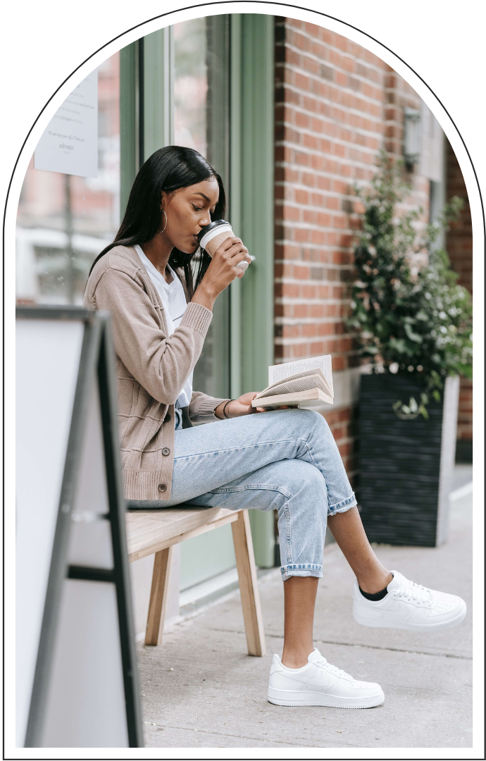 Woman reading a book and drinking coffee while sitting outside a café