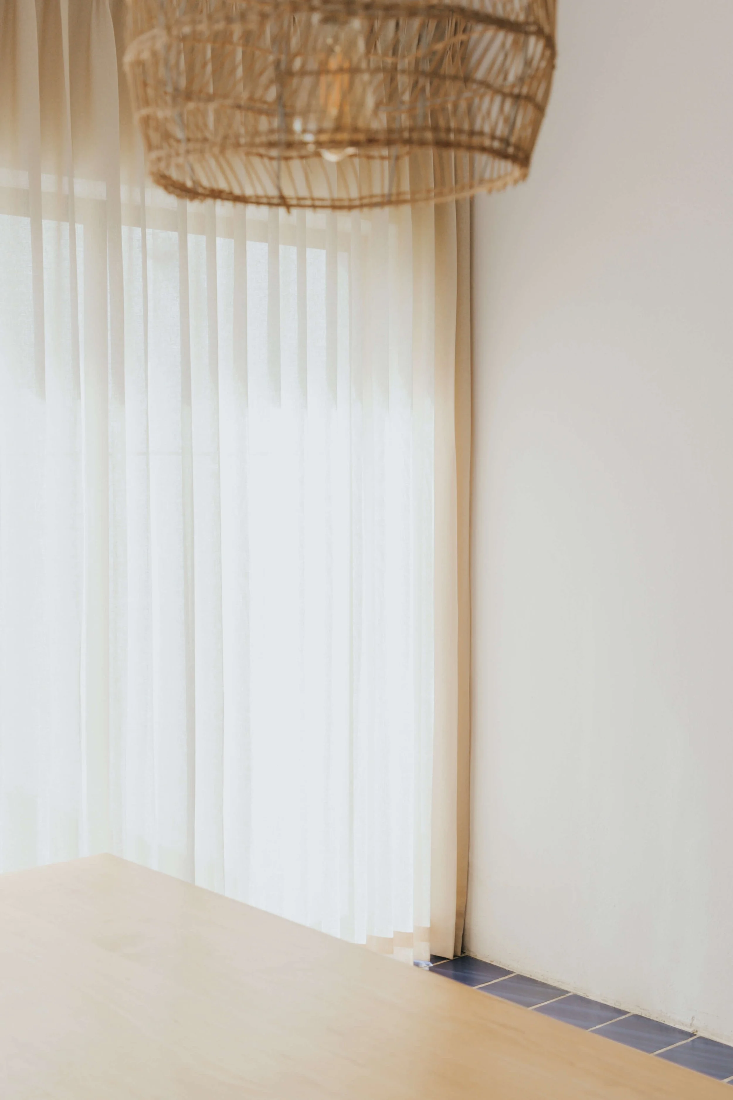 Close-up of a woven pendant light in front of sheer white curtains and a bright window