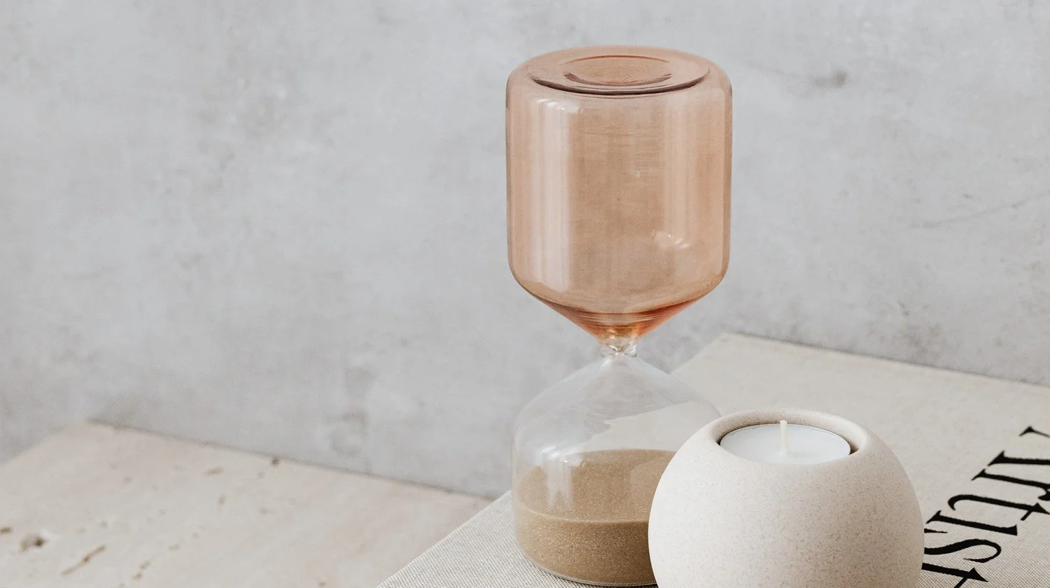 Minimalist home decor with an hourglass and white candle holder on a tabletop