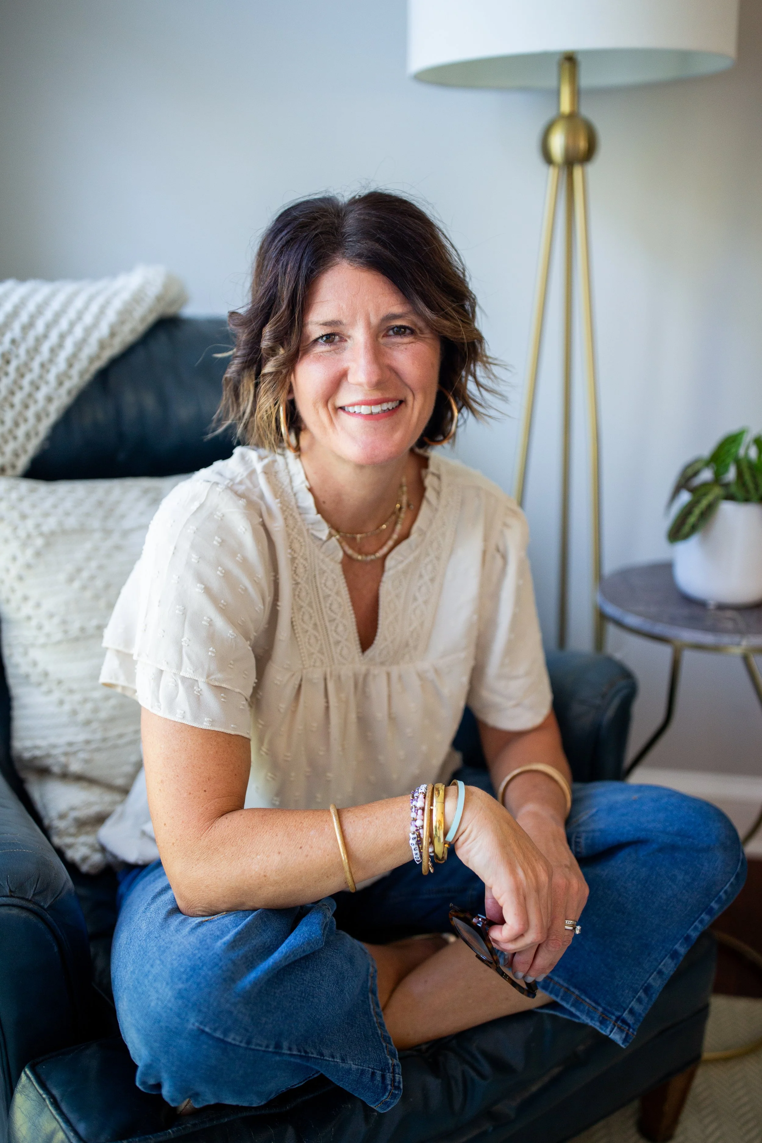 Smiling woman in a white blouse and jeans sitting on a sofa in a cozy living room