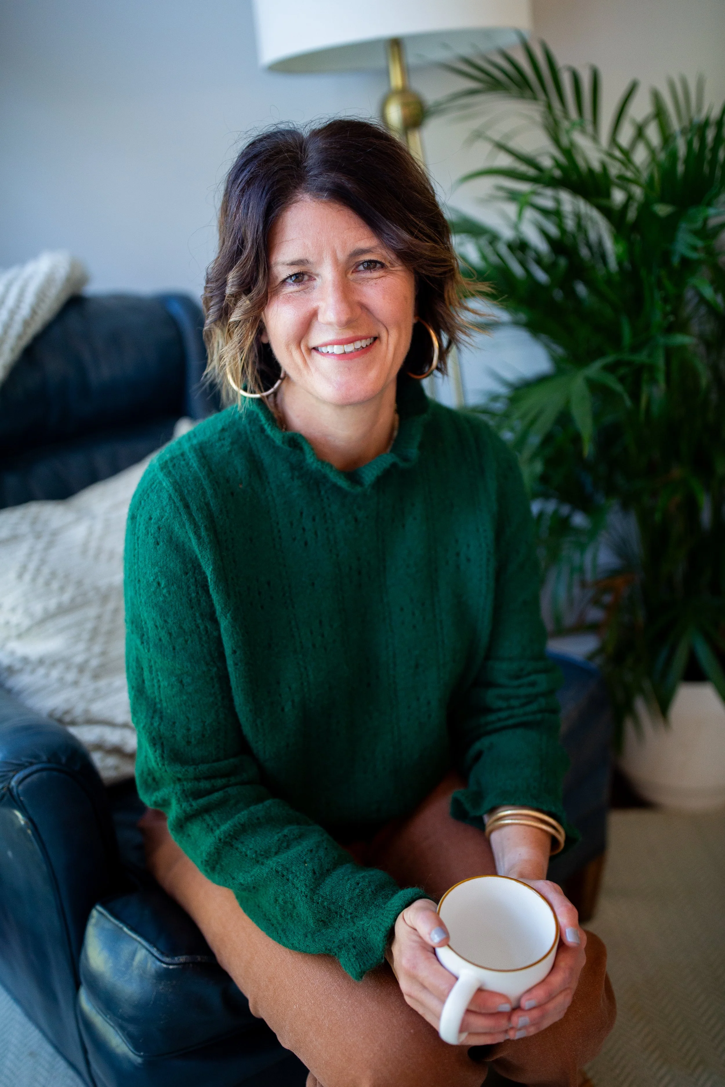 Smiling woman in a green sweater holding a white coffee mug at home