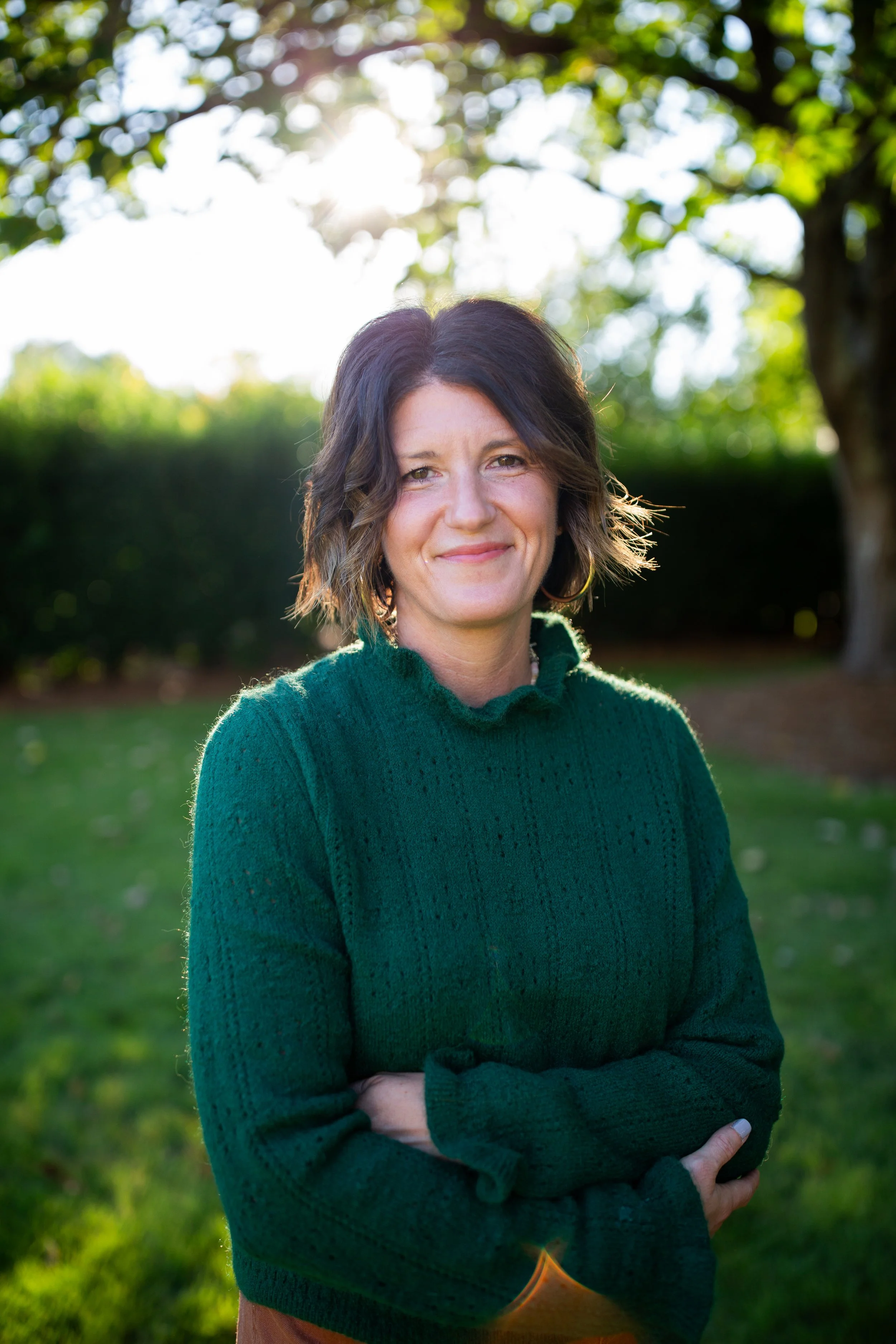 Smiling woman in a green sweater standing outdoors in a sunlit park