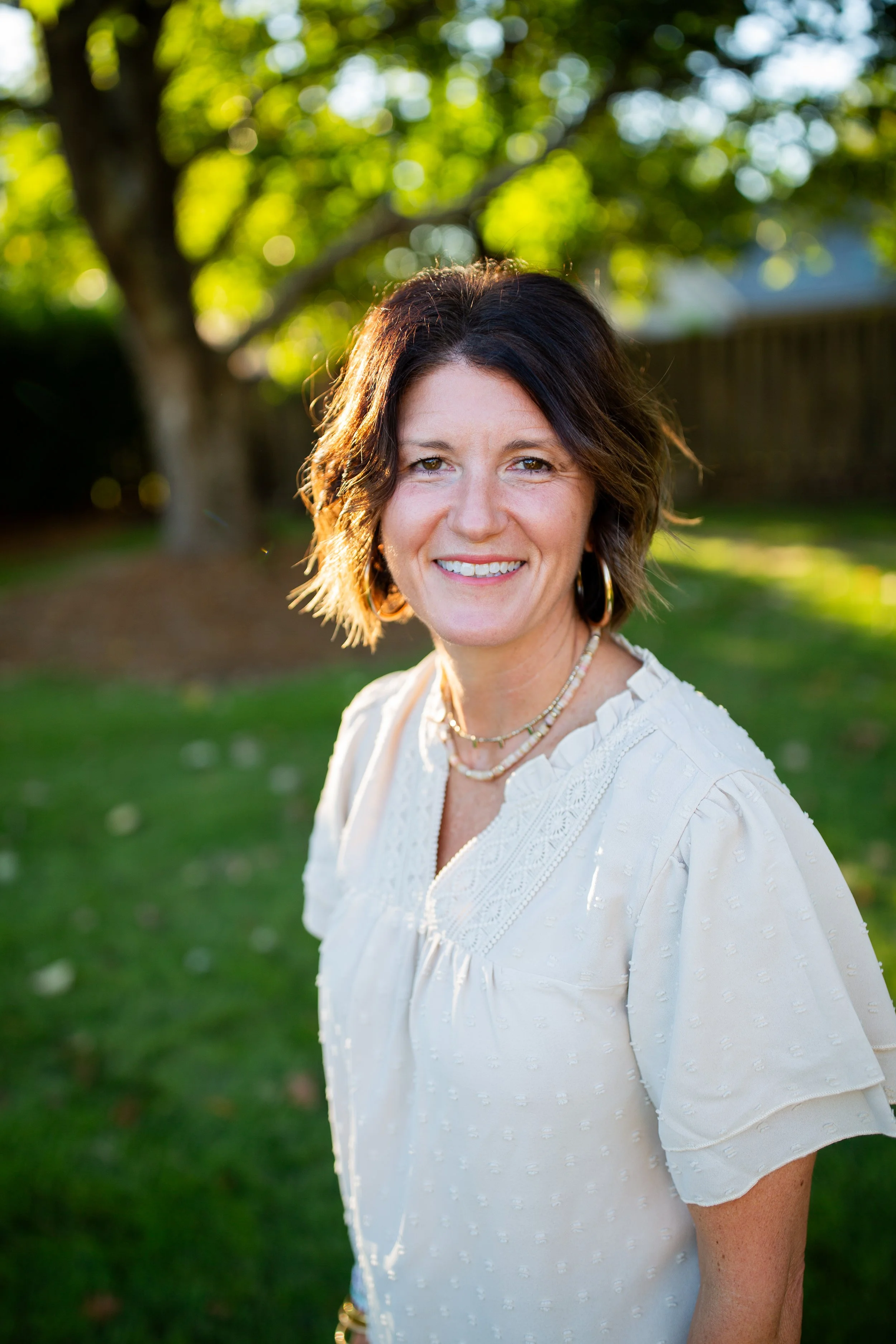 Smiling woman in a white blouse standing outdoors in a sunlit garden