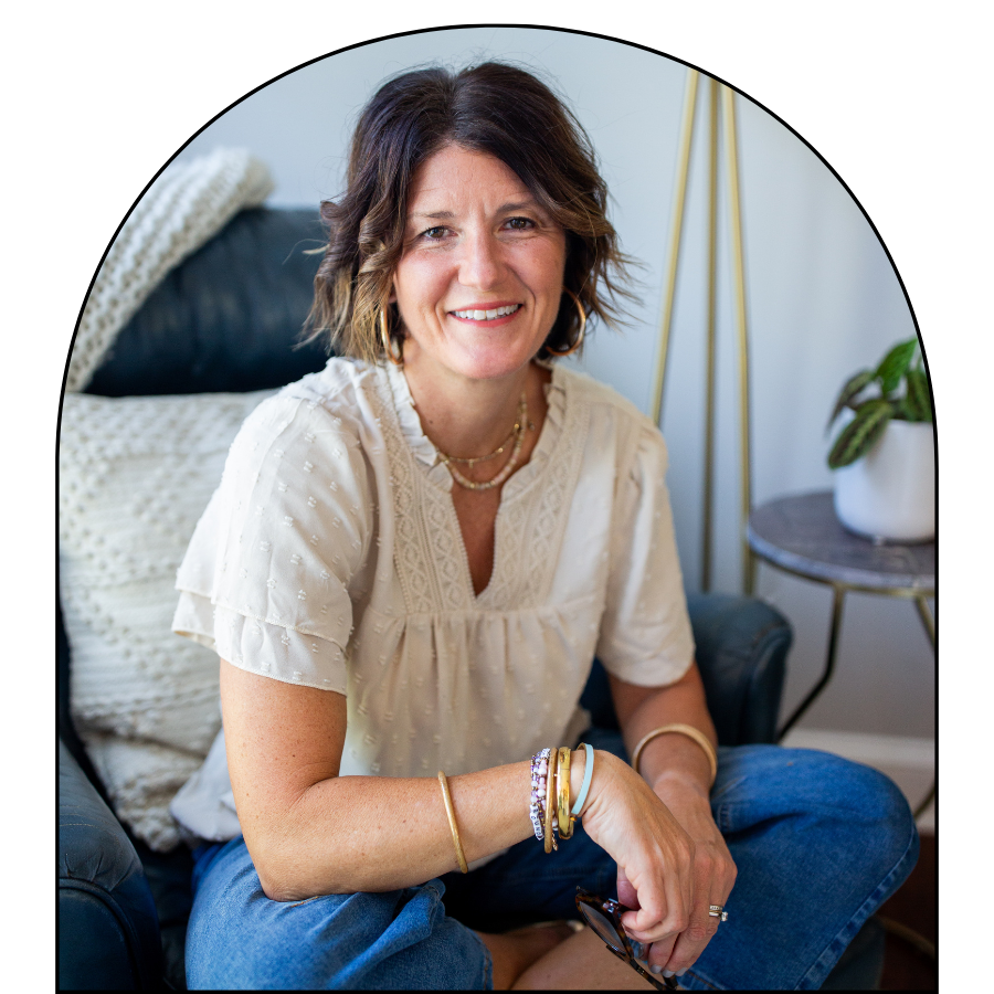 Smiling middle-aged woman in a white blouse and jeans seated in an armchair at home