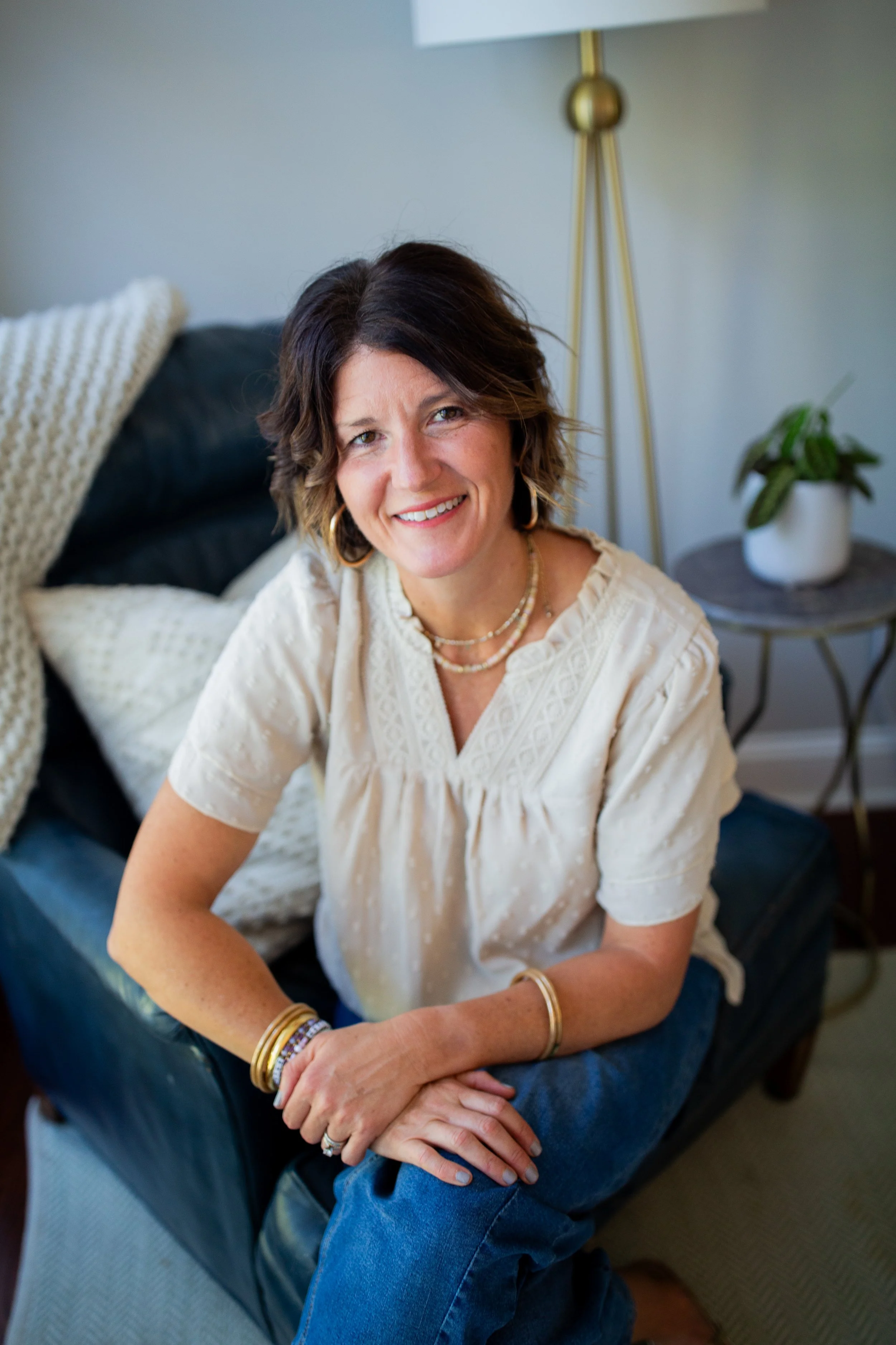 Smiling woman in a white blouse sitting indoors with her arms crossed over her knees