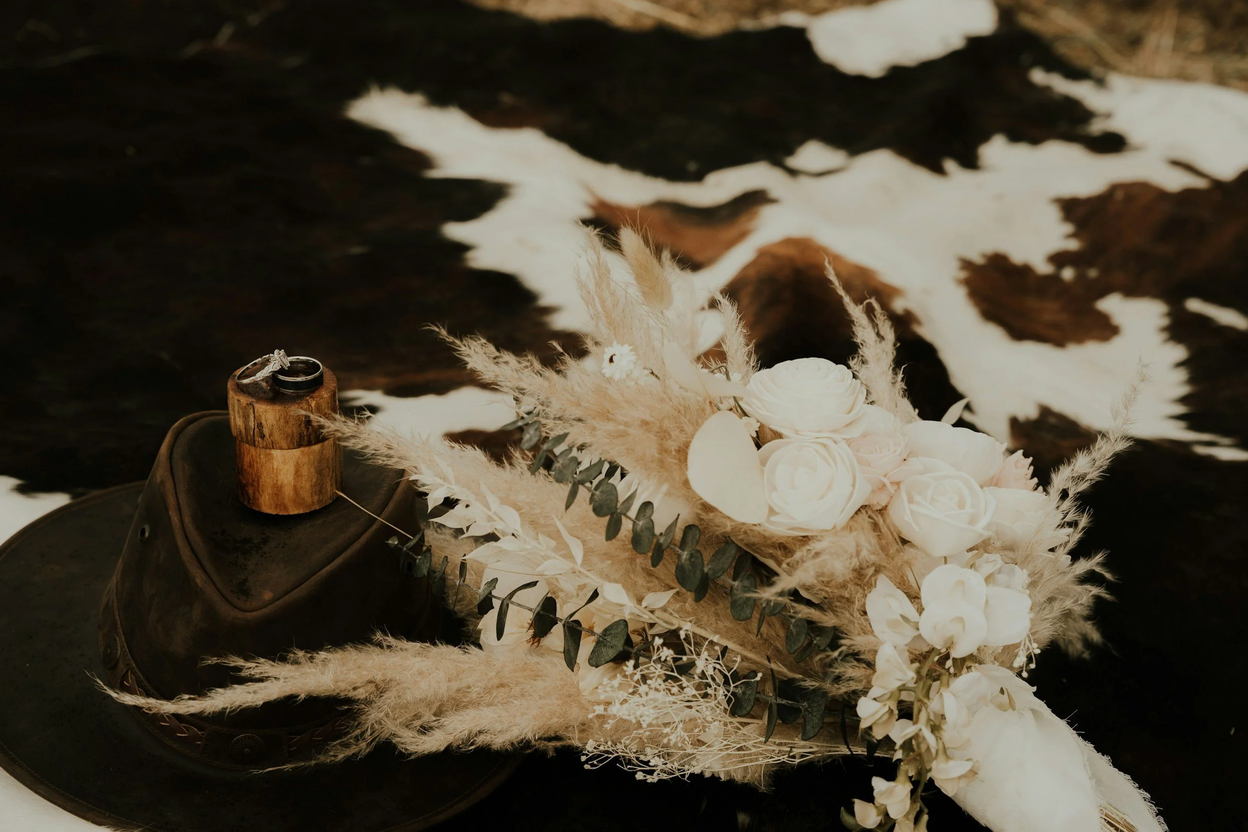 A pair of wedding rings on a piece of wood with flowers and greenery, placed on a metal shoe and black surface.
