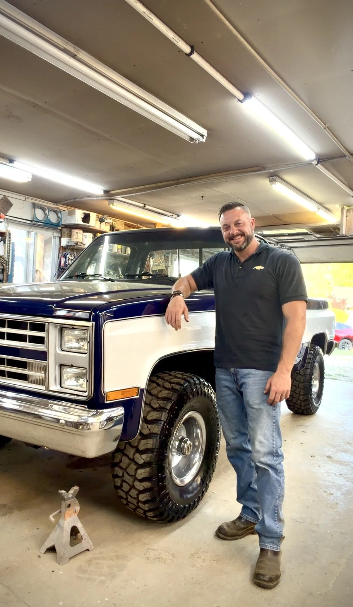 Chris Stiltner of Signature Series Motor Company standing next to a vintage blue and white pickup truck in a garage or workshop.