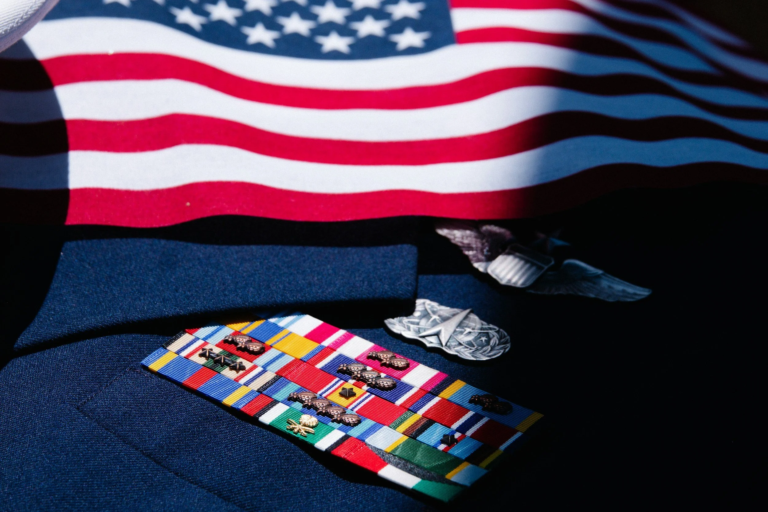 Close-up of a table display featuring a United States flag, a navy blue item, and various military medals and ribbons arranged on a plaid fabric.