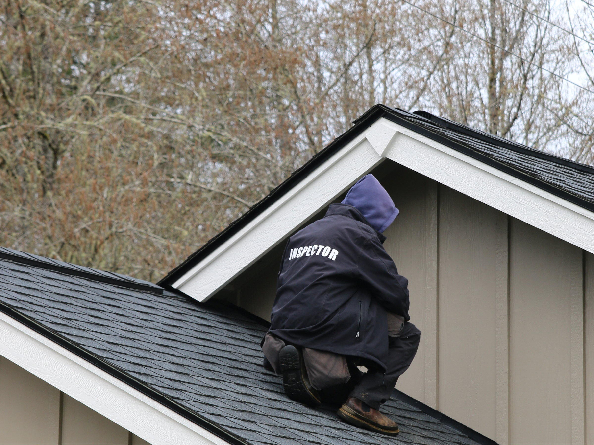 A home inspector on a roof in Montesano WA inspecting on a cold day with trees in the background.