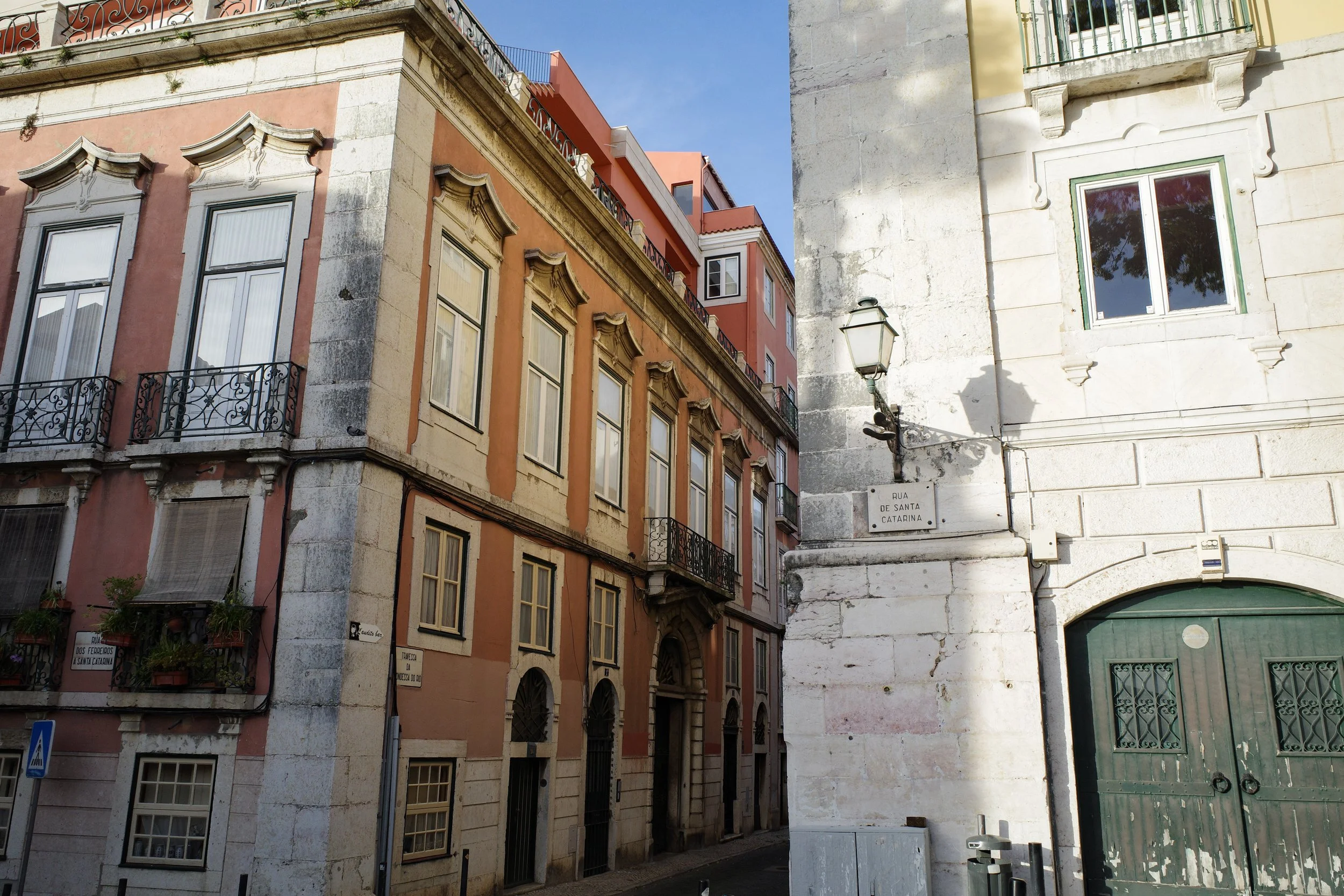 Colorful historic buildings with ornate window frames and wrought-iron balconies on a sunny street in Portugal, with a street sign reading 'Rua de Santa Catarina' and a traditional street lantern.