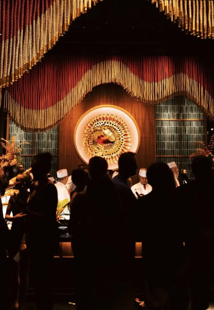 People gathered in a restaurant with a dragon emblem on the wall, decorated with colorful, layered fabric and warm lighting.