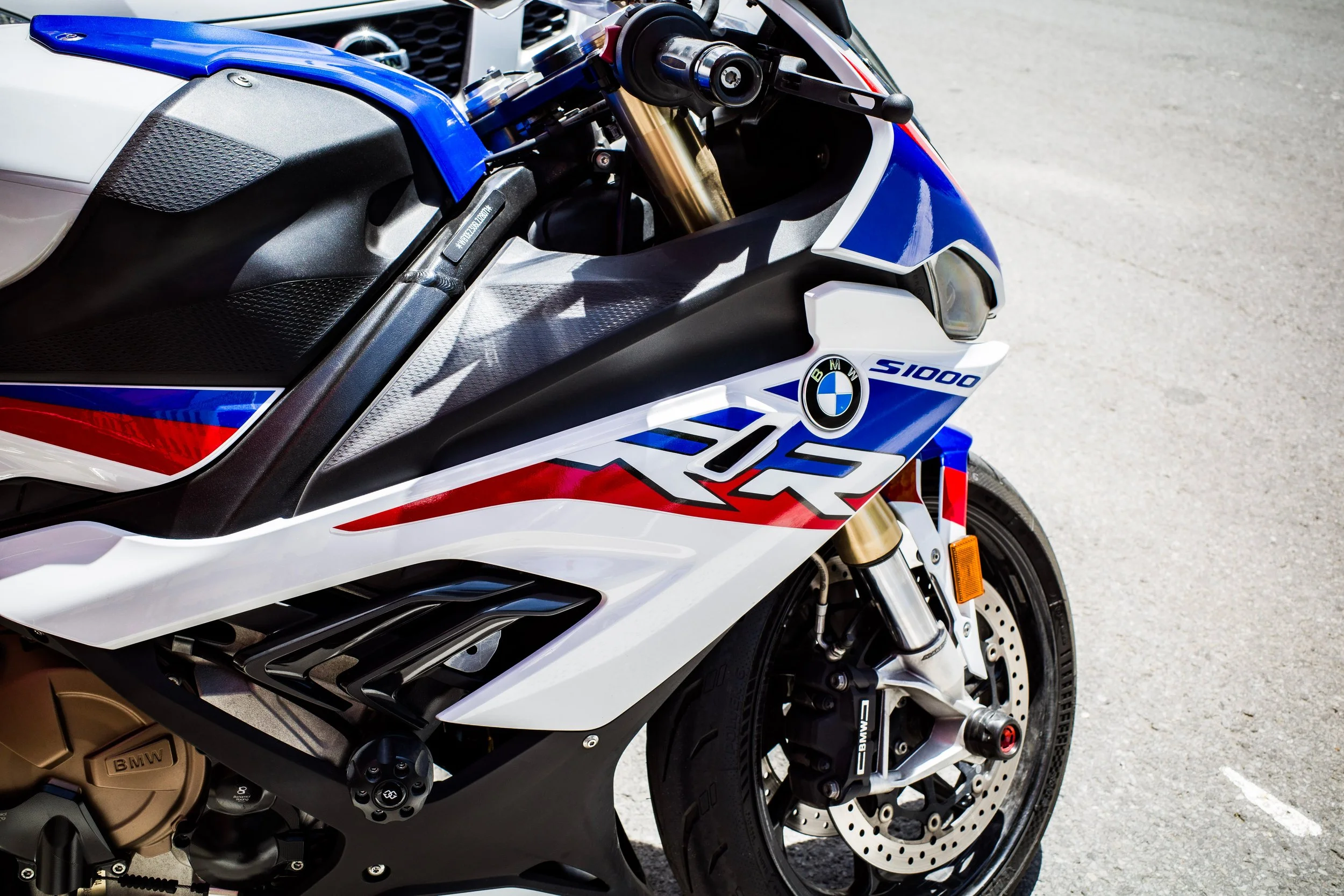Close-up of a BMW S1000 motorcycle, showing the front wheel, suspension, and partial bodywork with BMW and racing stickers, parked on a concrete surface.