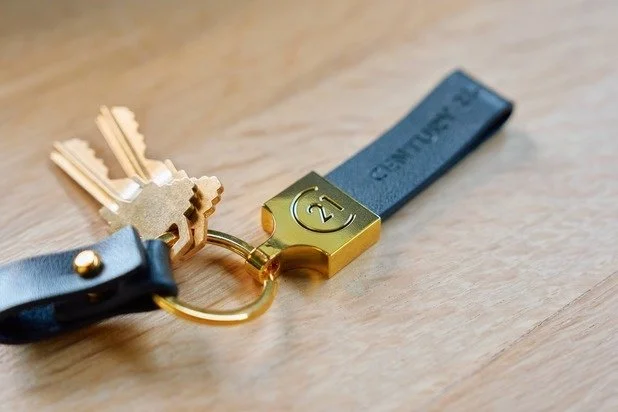 A set of keys attached to a black leather keychain, with a gold 21 film reel engraved on it, resting on a wooden surface.