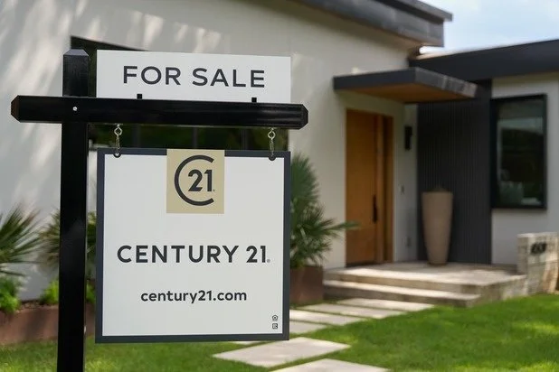 For sale sign in front of a modern house, featuring the Century 21 real estate logo and website.