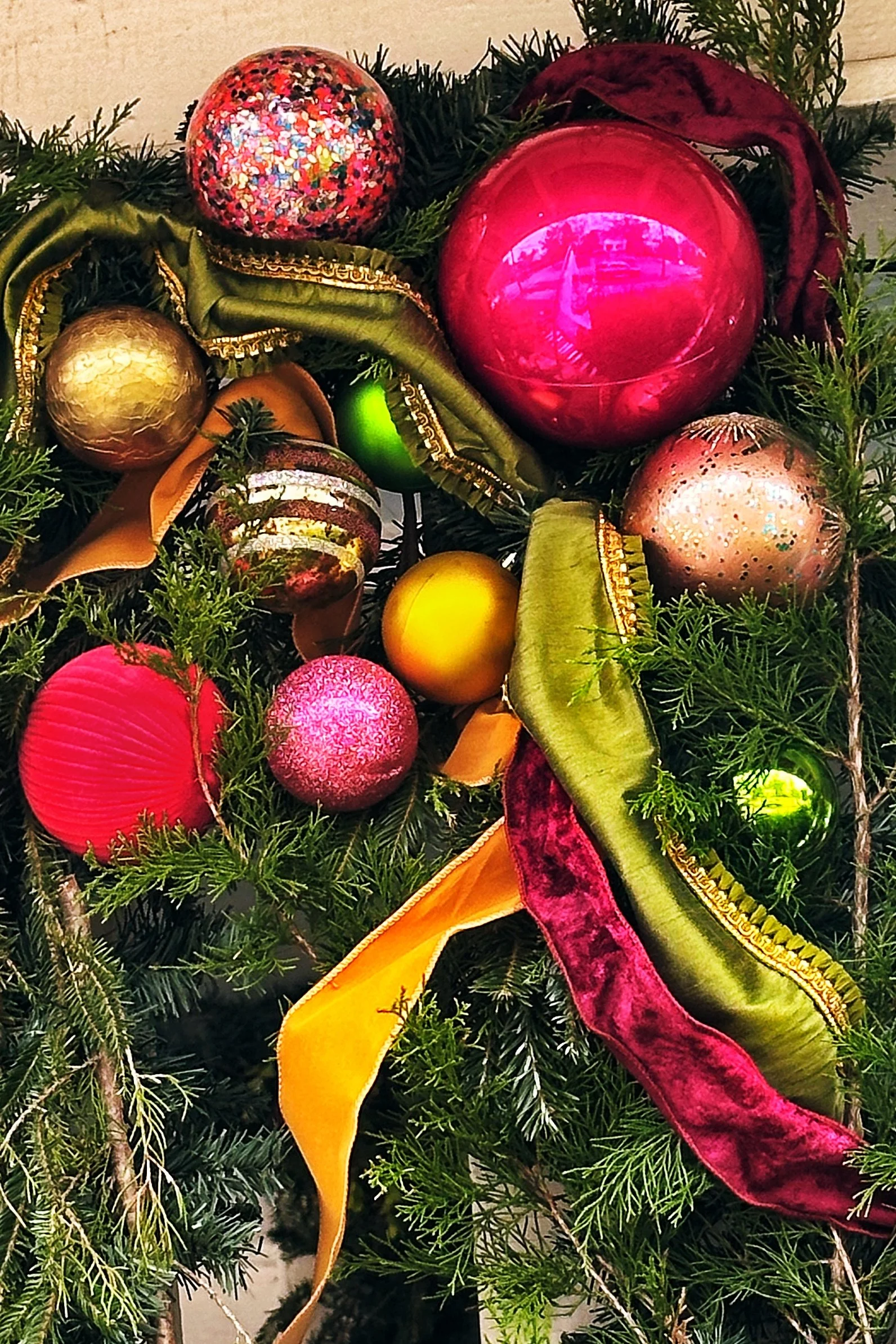 Moody Christmas porch garland featuring a hot pink, gold and olive ornament cluster with velvet ribbon woven through cedar