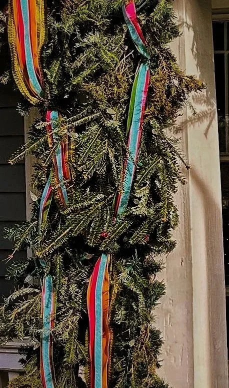 Striped ribbon running flat and straight down a garland-wrapped porch column, an example of ribbon that isn’t tucked