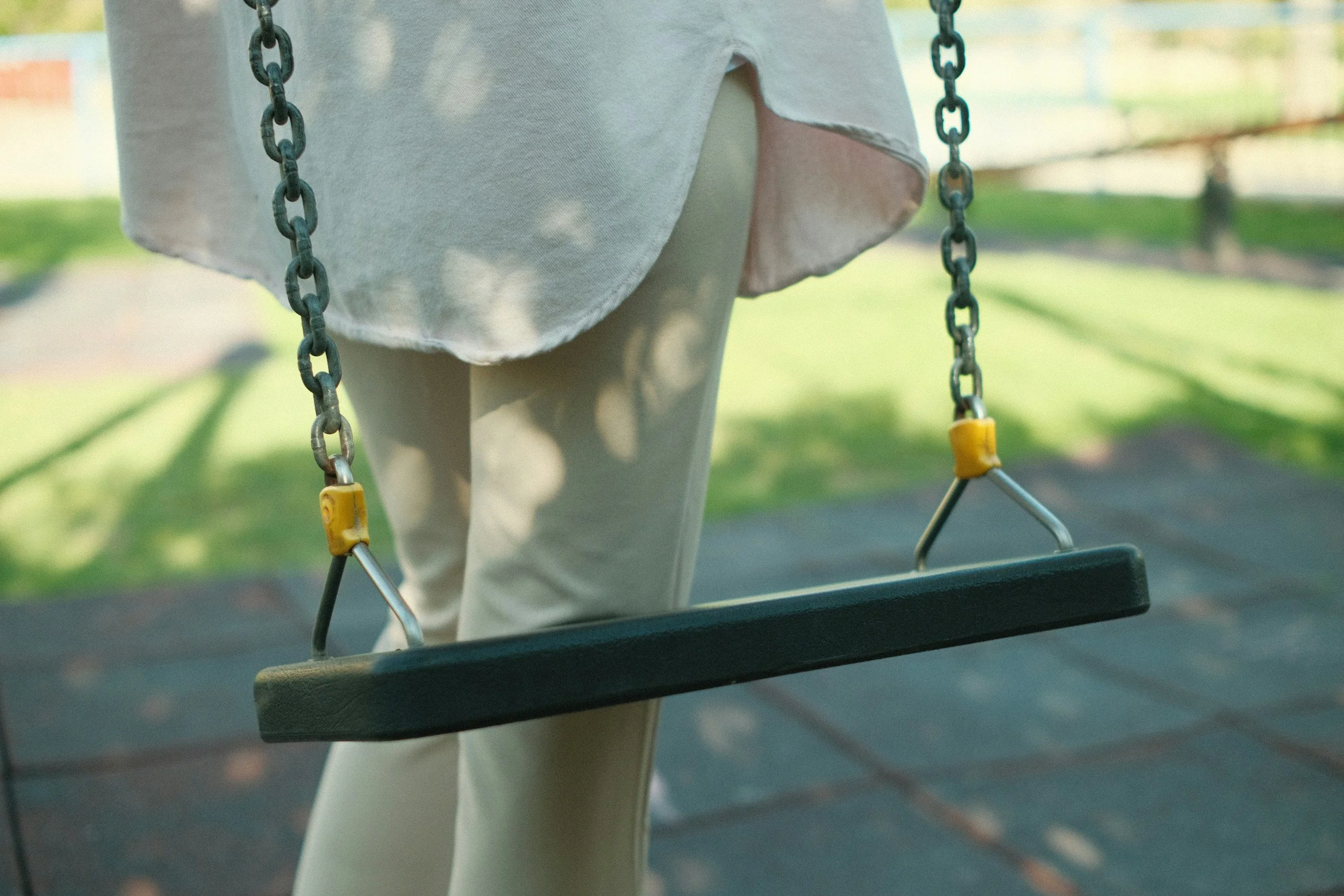 Close-up of a child's legs and a swing set in a park with green grass and blurred background.
