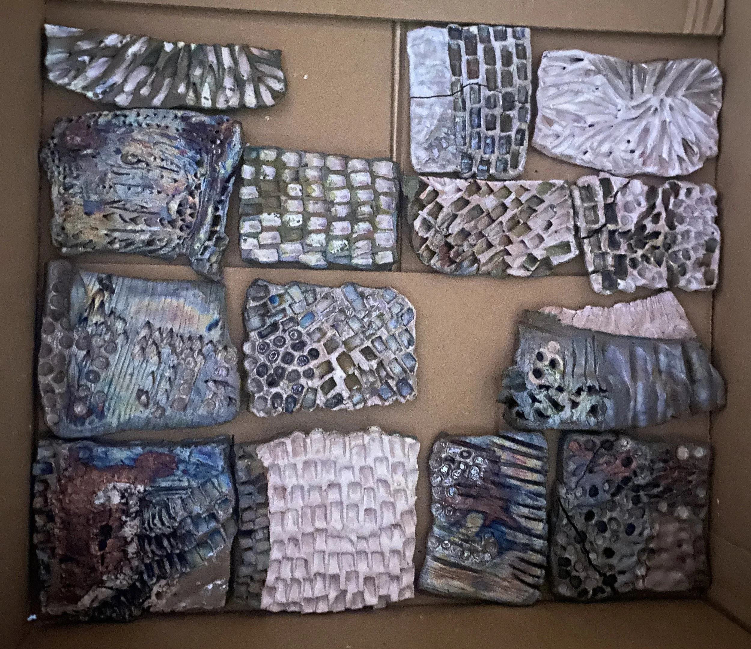 Multiple pieces of seashell and abalone shell art, each with various intricate patterns and natural iridescent colors, displayed on a cardboard surface.