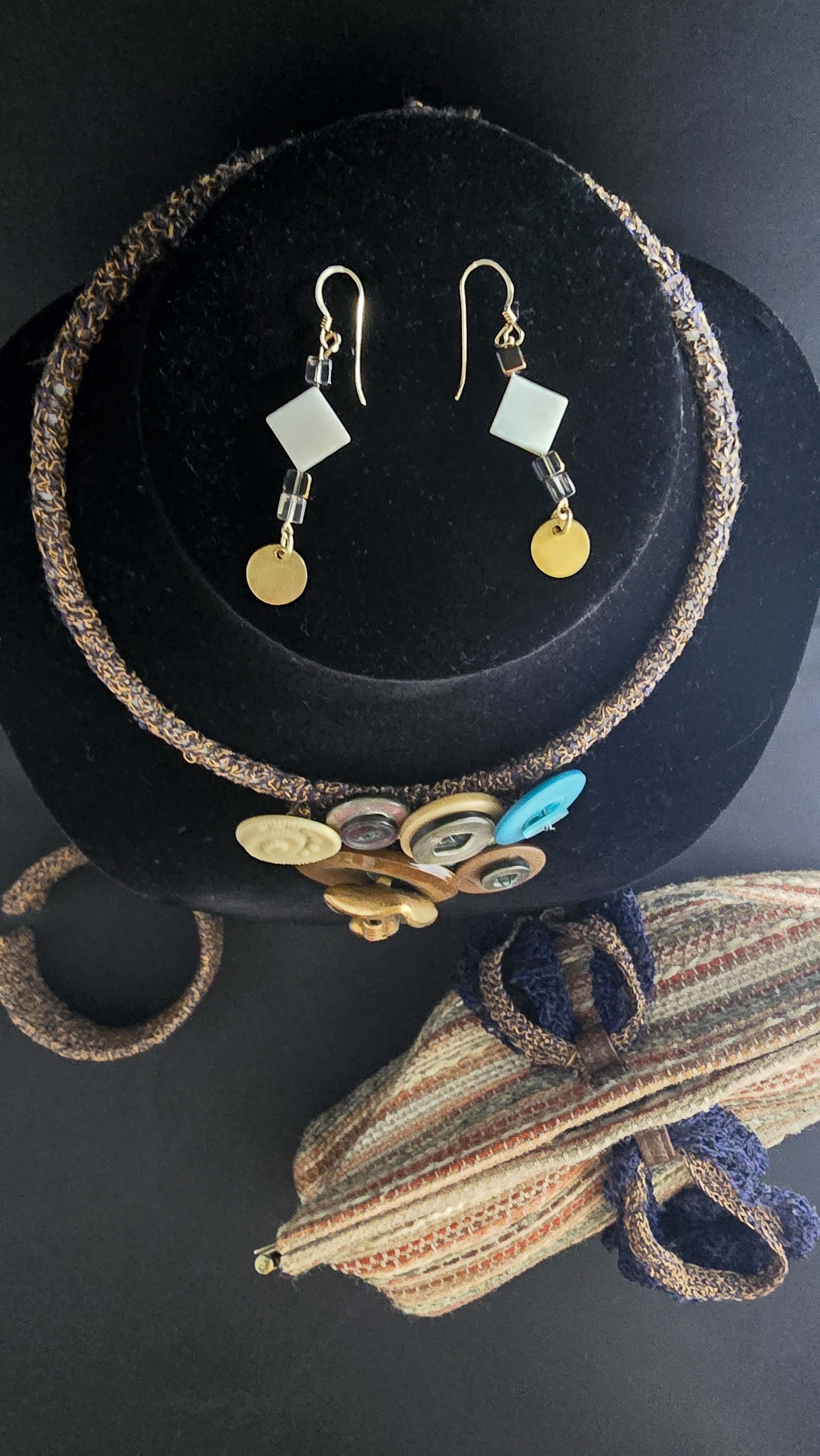 A display of jewelry including earrings, a necklace, and a fabric bag, set on a black surface.