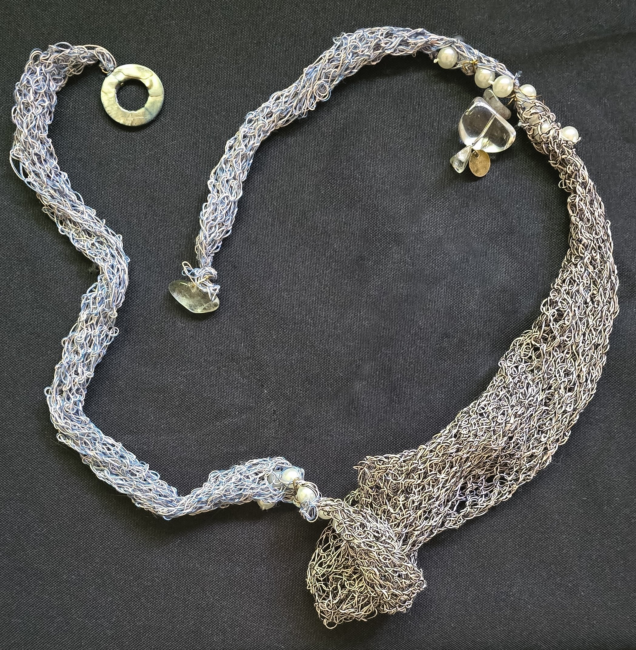 Confluence

Confluence is a one-of-one wearable work constructed through the accumulation and intertwining of linear elements. Mother-of-pearl, glass beads, and simulated pearls move through cotton-blend thread, creating a shifting, sculptural form t