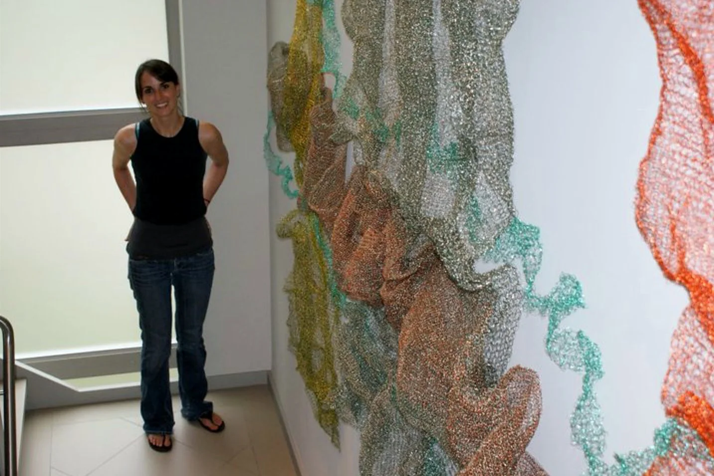 A woman standing next to a large abstract colorful art installation on a white wall.