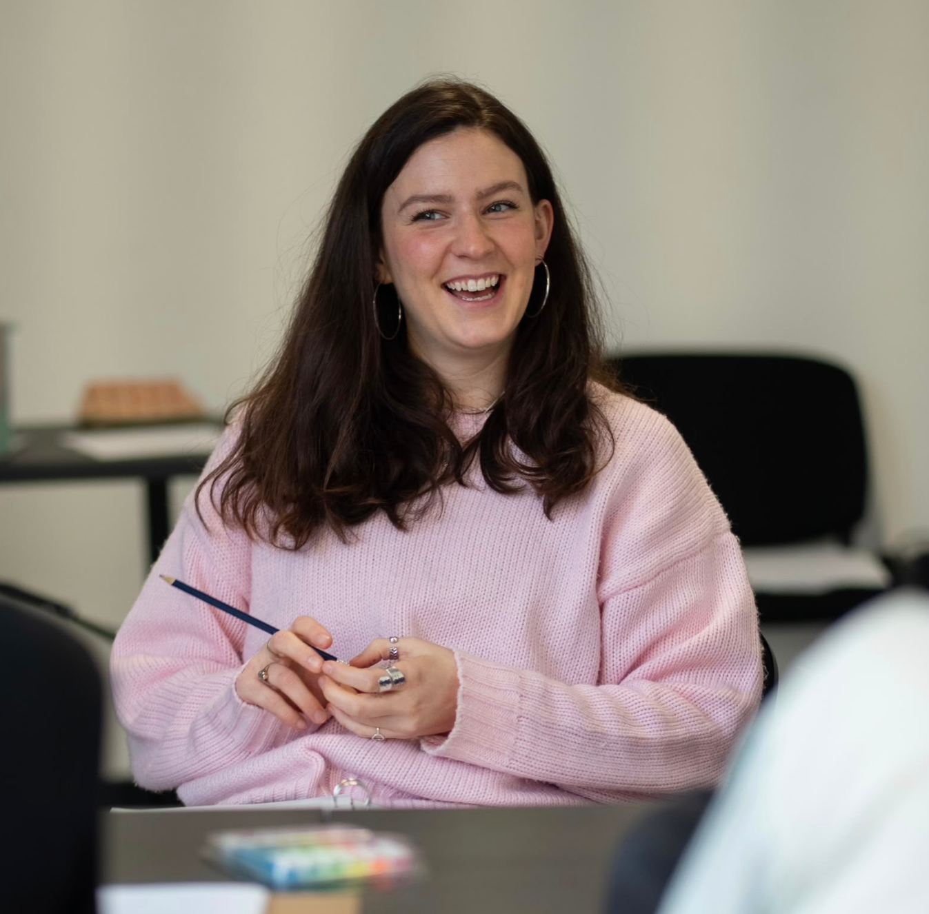 Chani Merrell in a rehearsal room. She is a white woman with medium length auburn  hair and a pink jumper on.