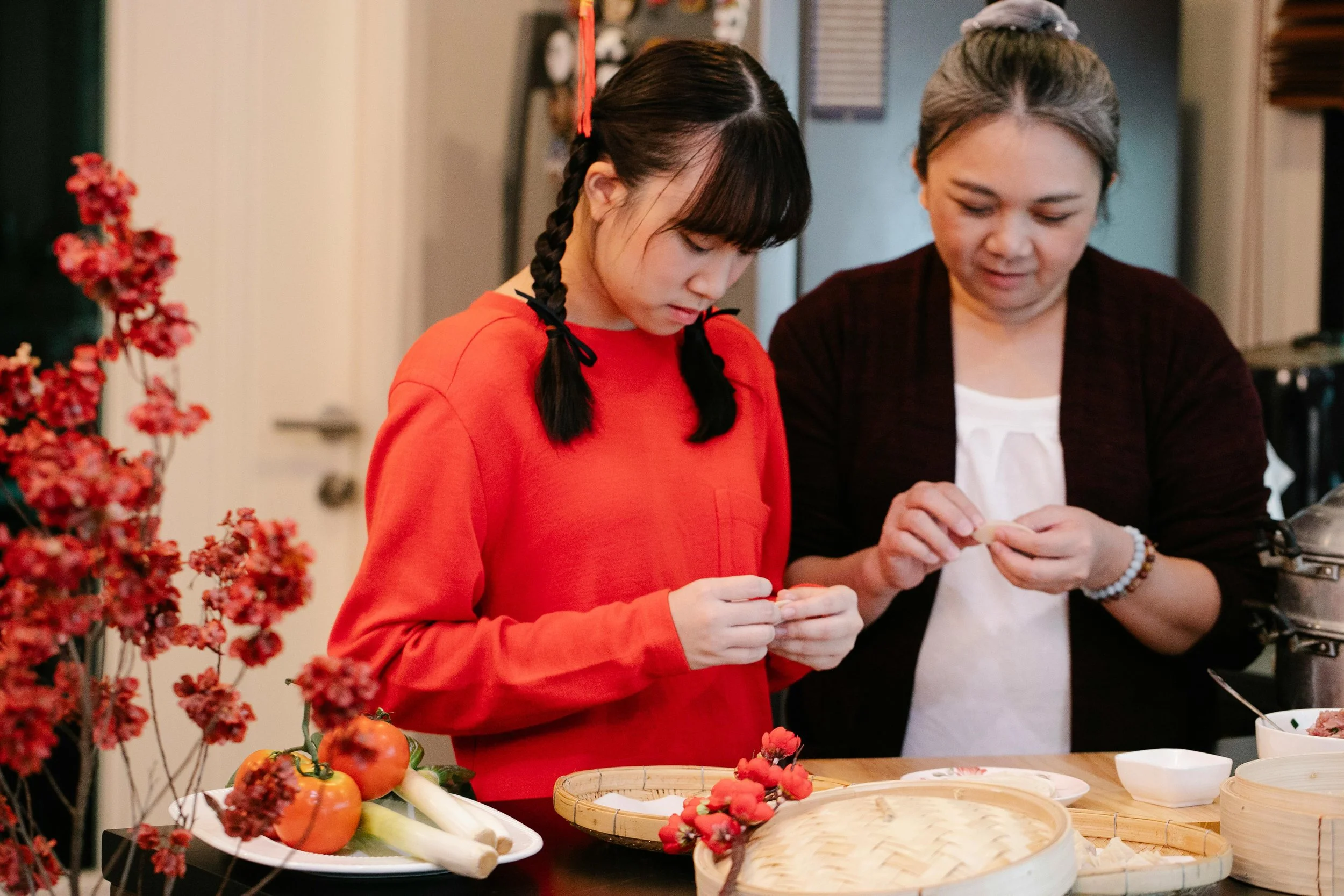Two women are preparing food together in a kitchen, surrounded by vegetables and dishes.