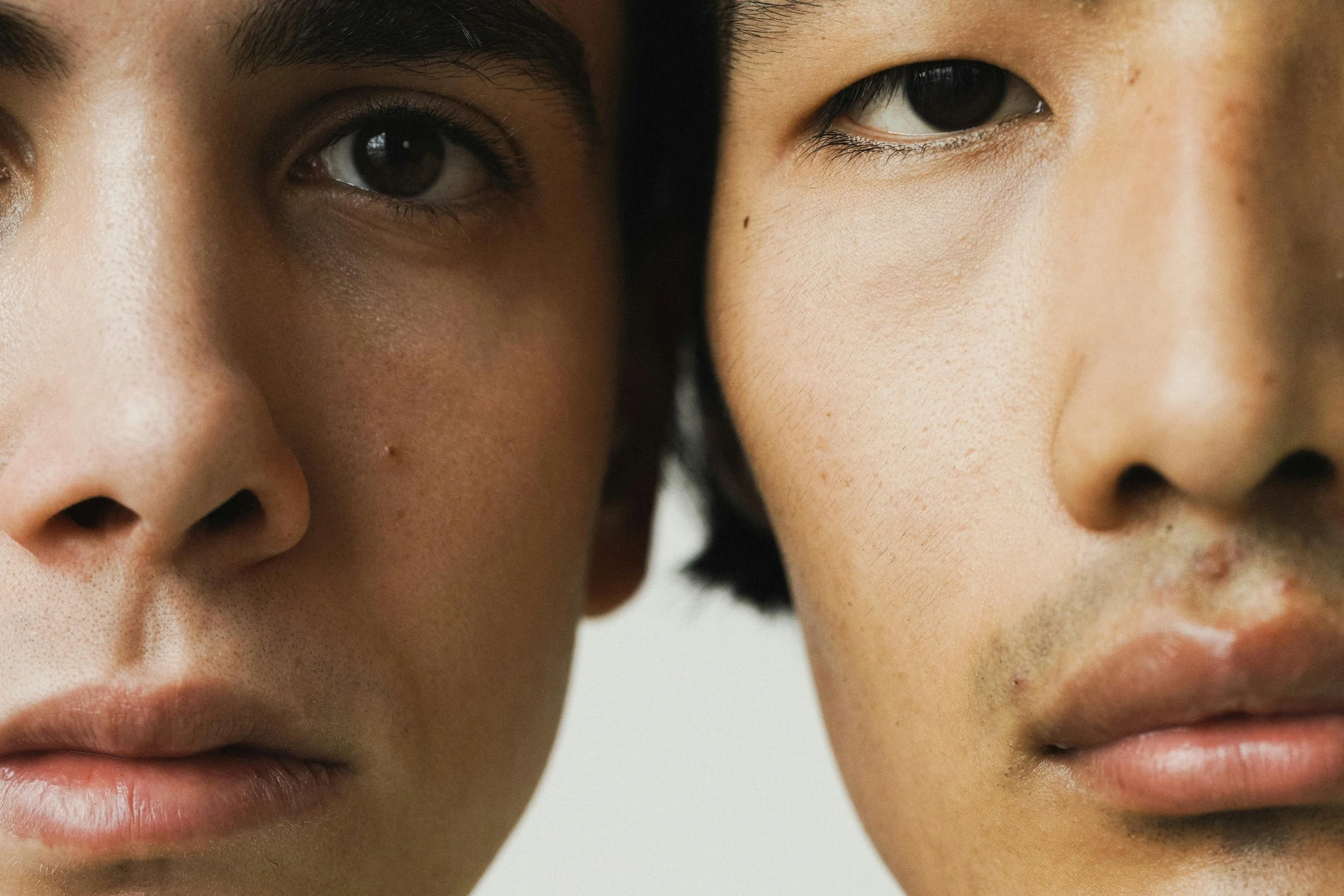 Close-up of the faces of two individuals, showing their eyes, noses, and part of their mouths, with a neutral background.