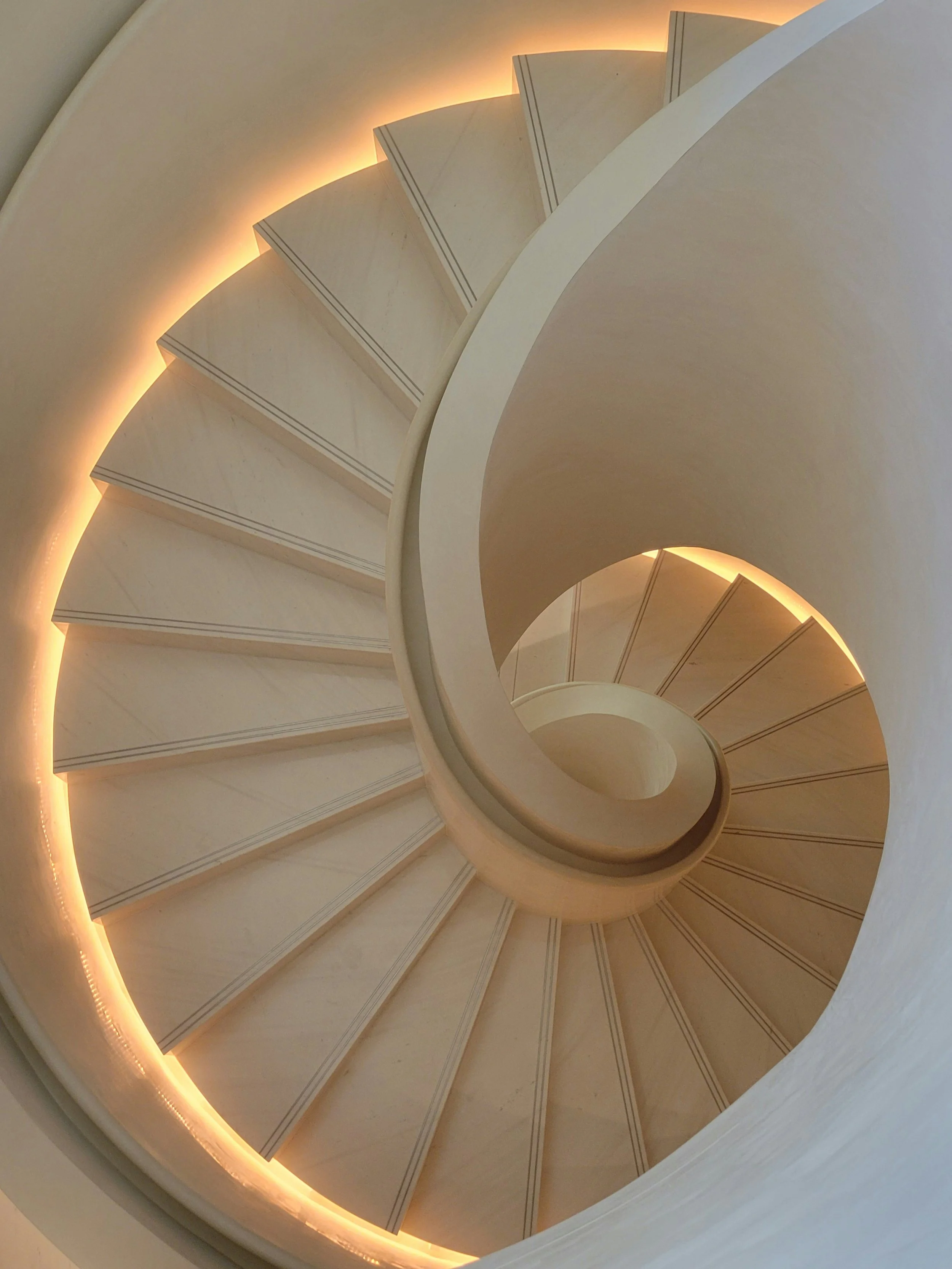 Spiral staircase viewed from above with warm lighting on the inner curve.