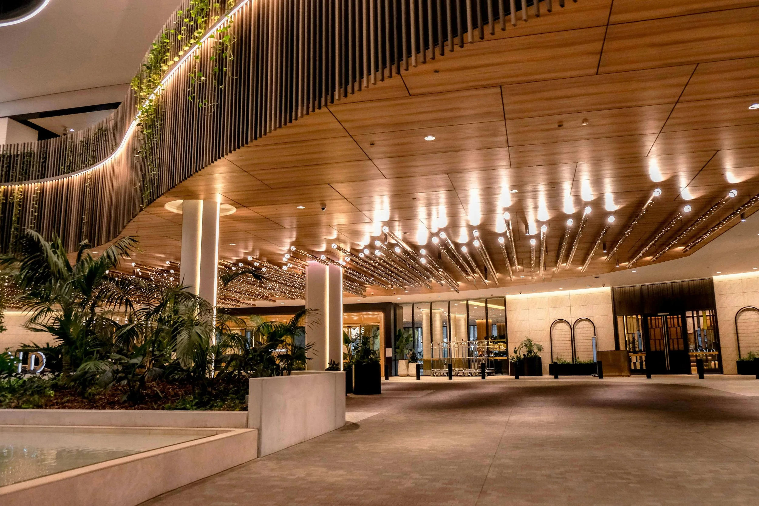 Indoor area with a wooden ceiling, modern lighting, and surrounded by plants and seating areas.