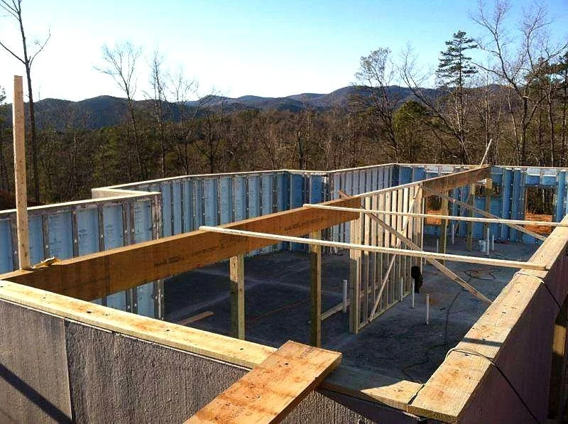 Construction site with wooden framing on top of a building, overlooking a scenic mountainous landscape with trees in the distance.