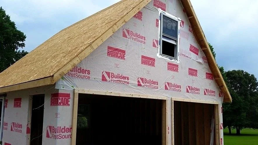 A house under construction with framing and exterior sheathing, showing a window and opening for a garage.