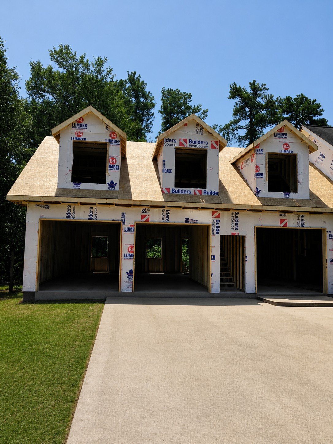 Two-story home under construction in Colorado with wood framing, three garage bays, dormer windows, and protective building wrap.