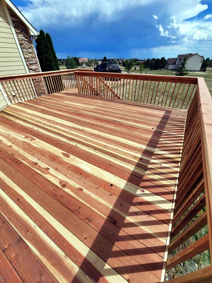 Wooden deck with railing, outside view of suburban neighborhood under partly cloudy sky.