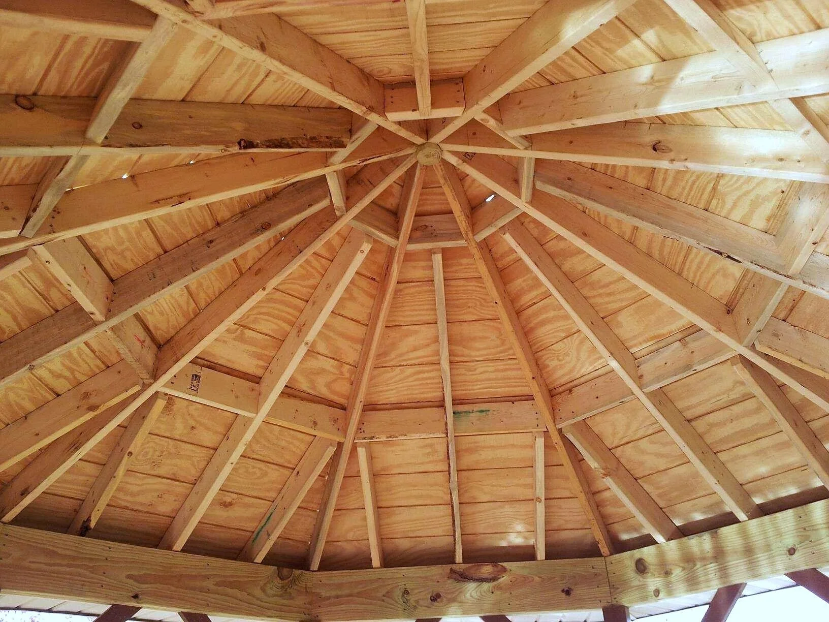 Inside view of a wooden gazebo or roof structure, showing the interior wooden beams and planks arranged in a circular pattern.