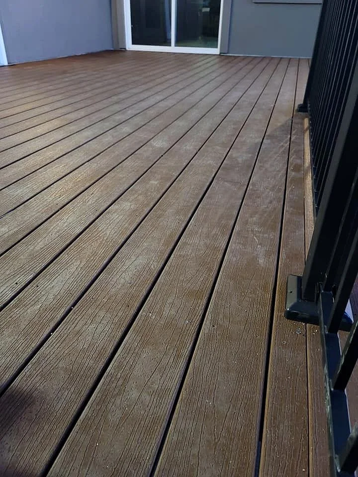 View of a wooden deck with a black metal railing on the right and a sliding glass door at the far end.