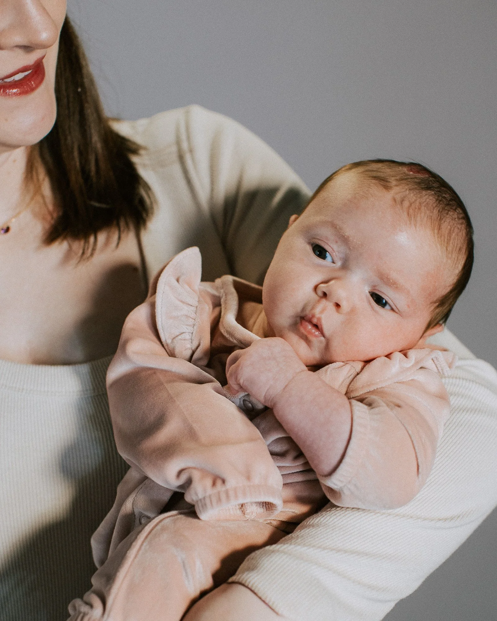 A woman holding a baby, both appearing to be in a close-up portrait, with only parts of their faces visible.