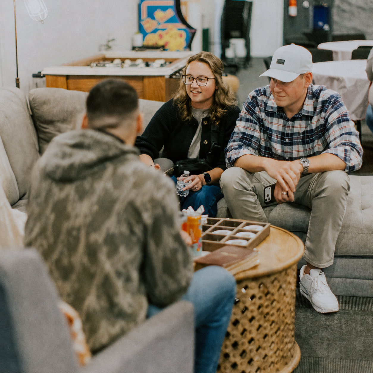 Group of four young adults talking and sitting on couches in a casual, cozy indoor setting.