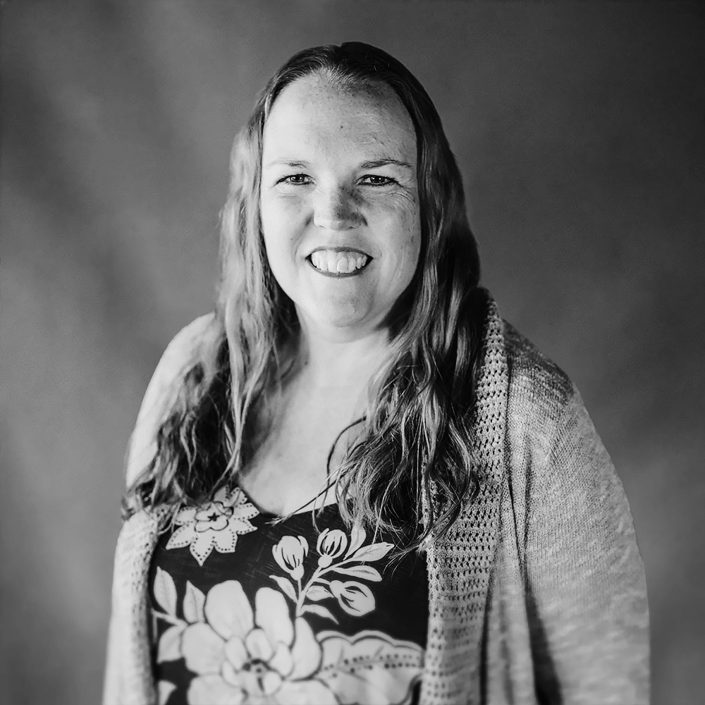 Black and white photo of a smiling woman with wavy hair wearing a floral top and a cardigan.