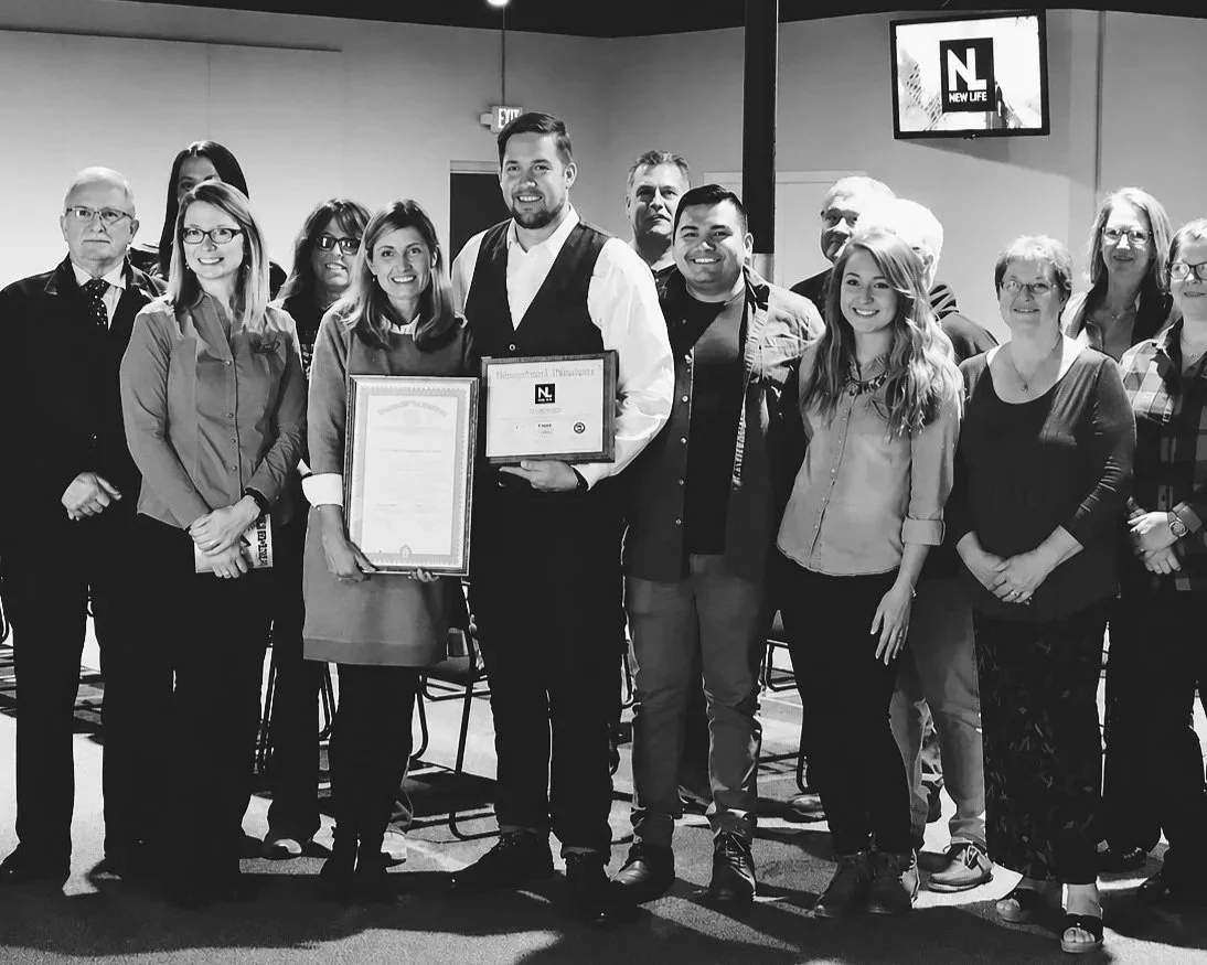 Group of people, including two holding framed certificates, posing together indoors for a photo at an award or recognition event.