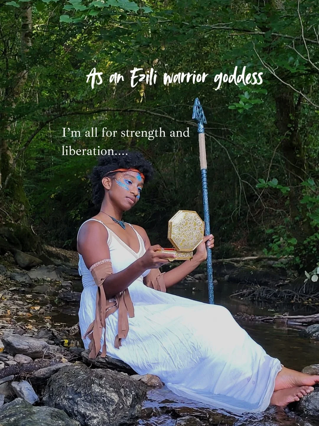 Mermaid Esili warrior goddess Andrina sitting on rocks by a stream in a forest, holding a decorative mirror and a spear, with face paint and jewelry, representing strength and liberation.