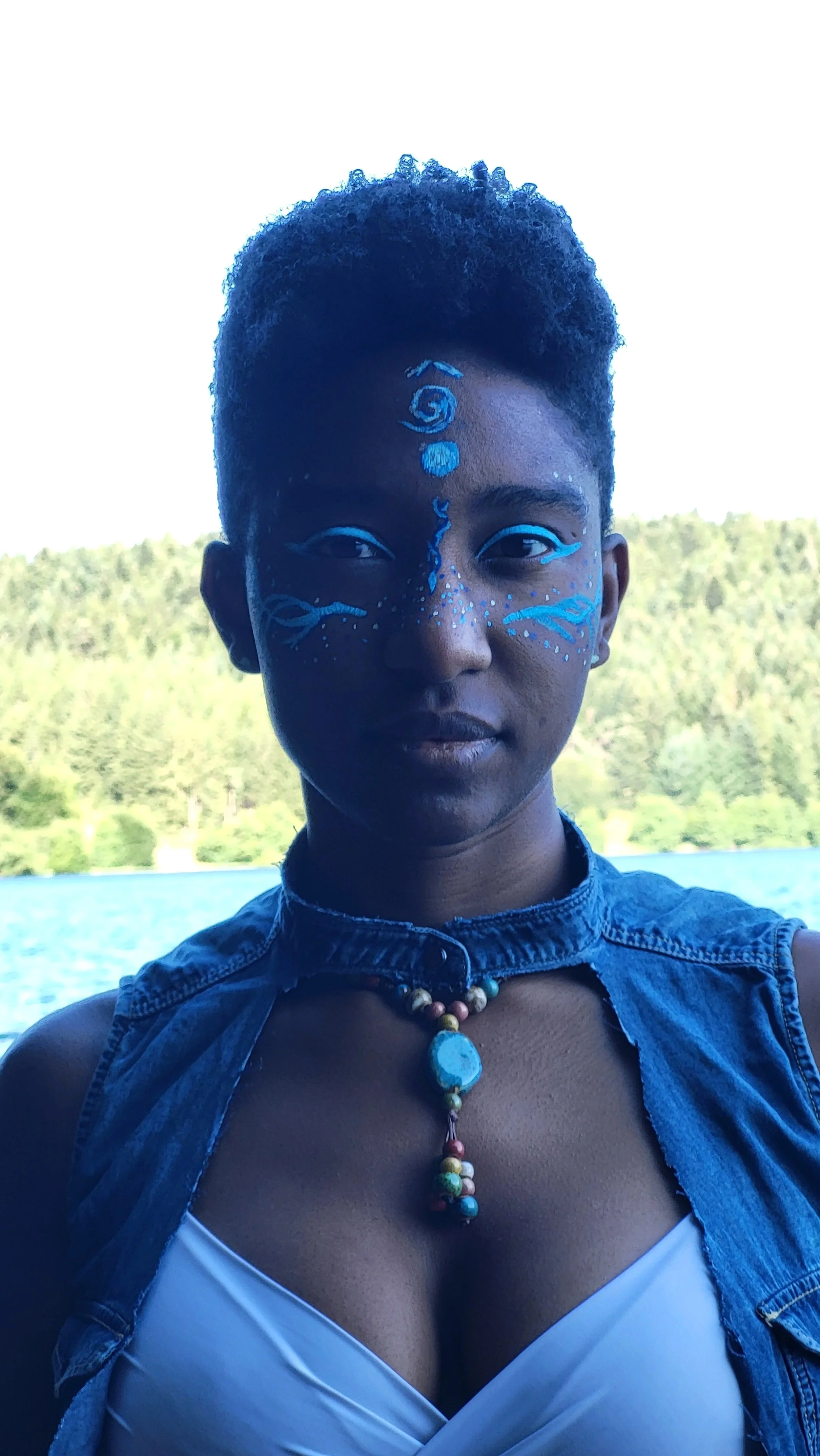 Mermaid Andrina faces camera for portrait shot and she is wearing blue warrior makeup and necklace of gemstones