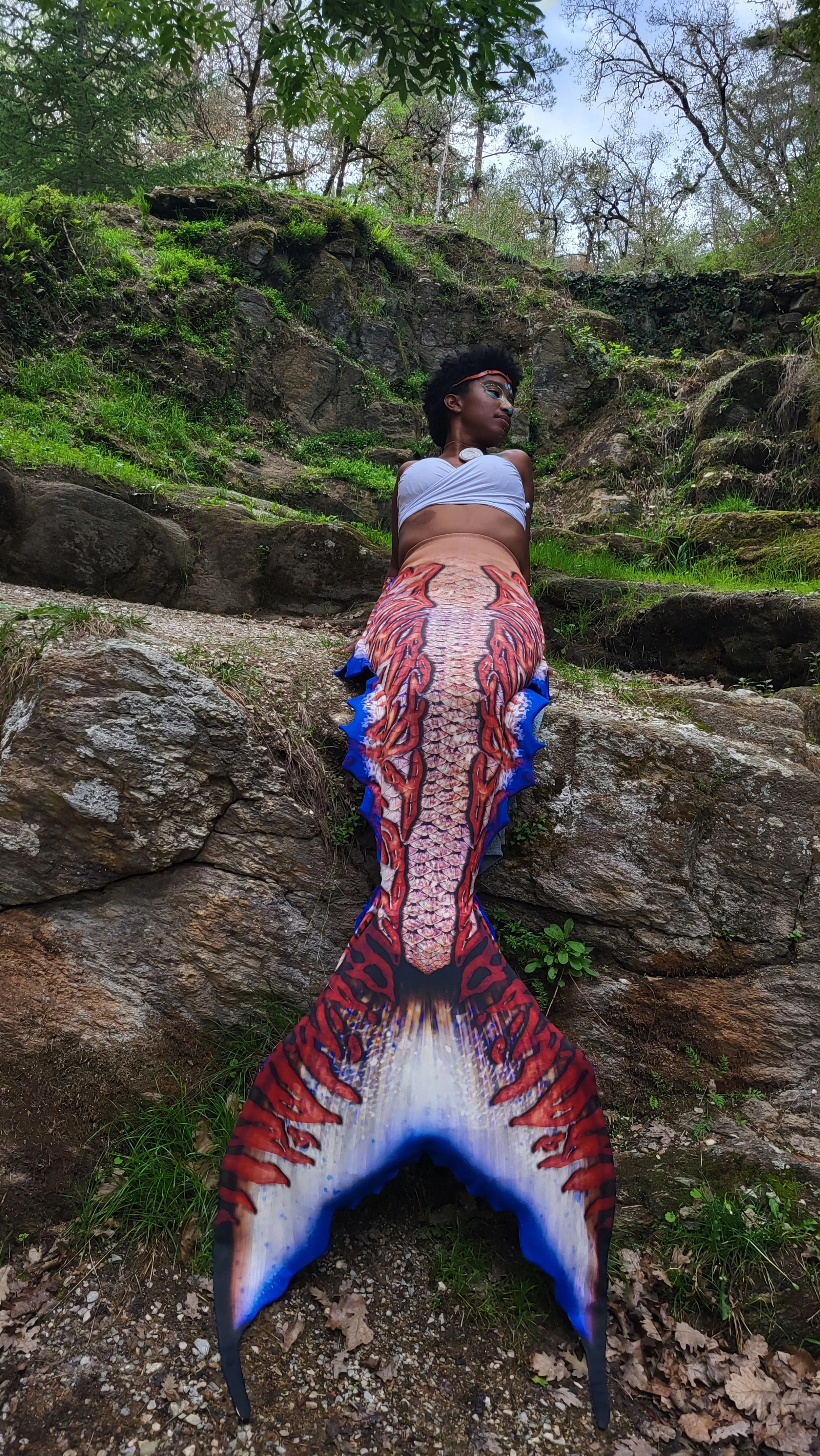 Mermaid Andrina  sitting on stone edge cliff in the forest