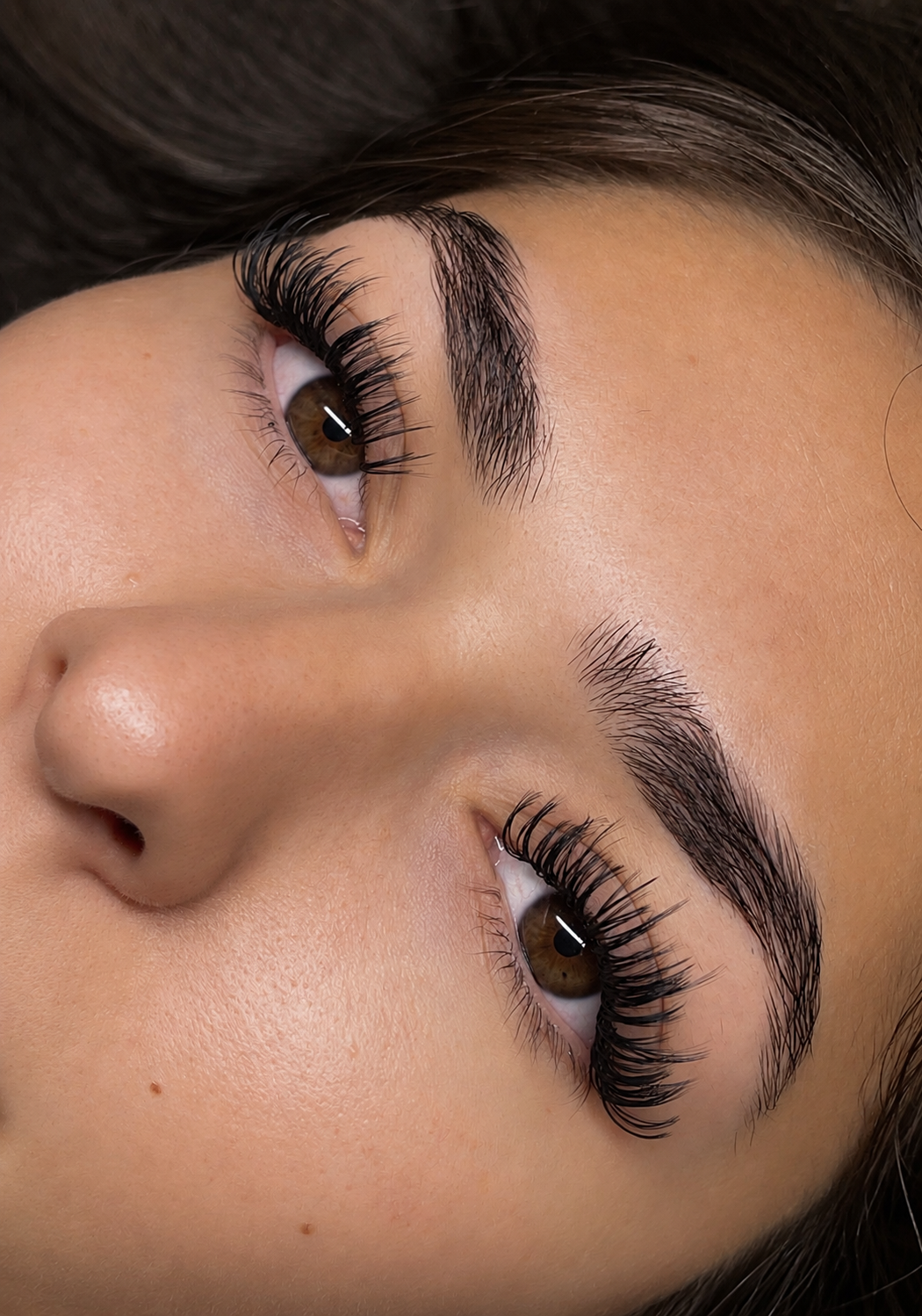 Close-up of a woman's face focusing on her eyes, showing long, thick eyelashes, well-groomed eyebrows, and clear skin.