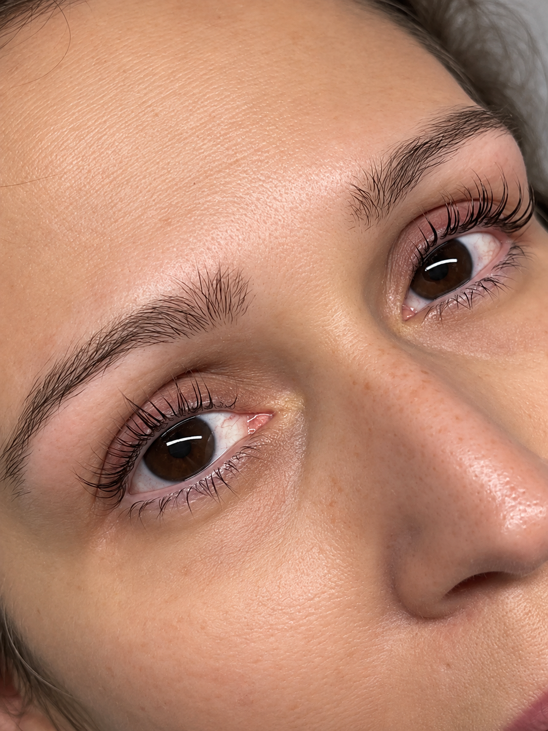 Close-up of a person's face focusing on brown eyes, eyebrows, and skin texture.