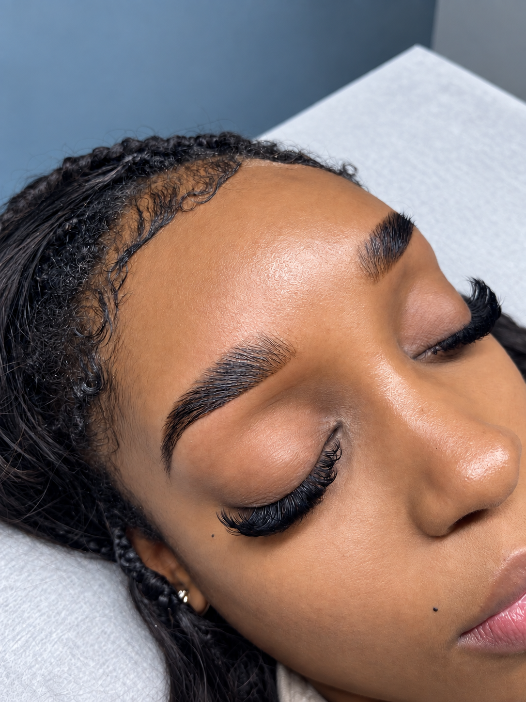 Close-up of a woman with freshly done eyelash extensions, organized eyebrows, and wet hair, lying on a white surface.
